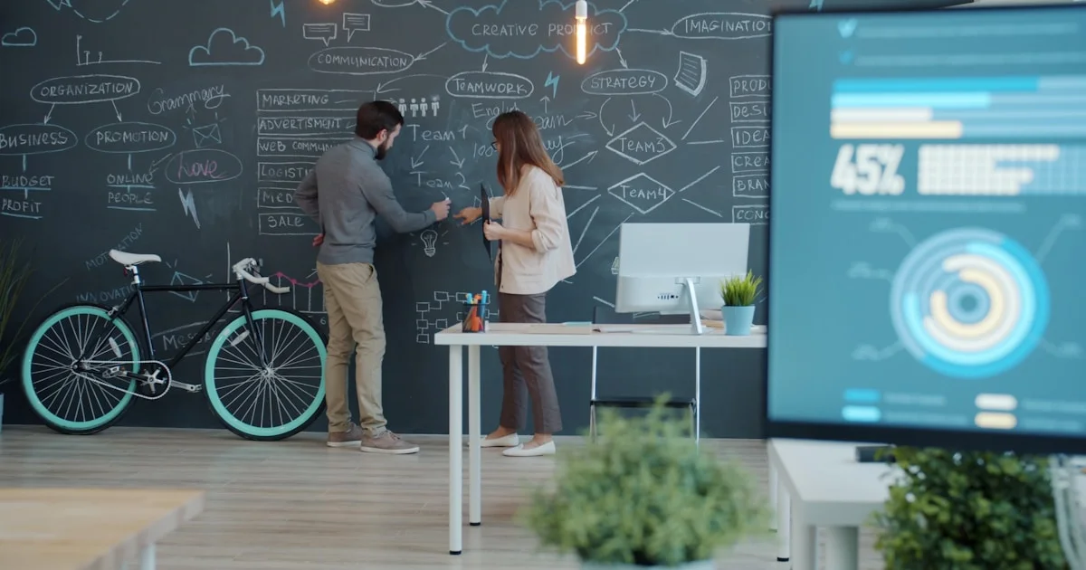 Two people collaborating on a chalkboard with a bicycle.