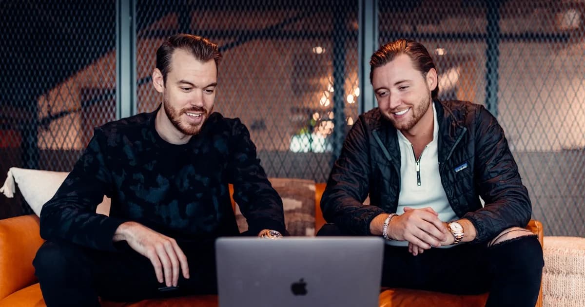 two men sitting at a table looking at a laptop