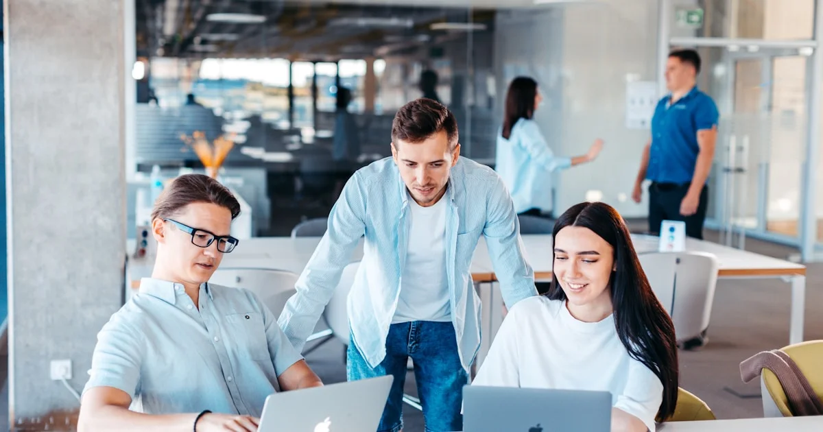 a group of people sitting around a table with laptops