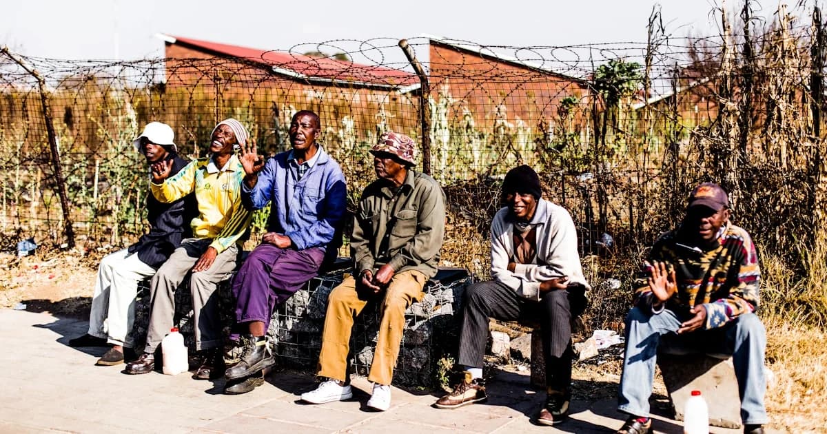six men sitting on bench in front barbed wire fence