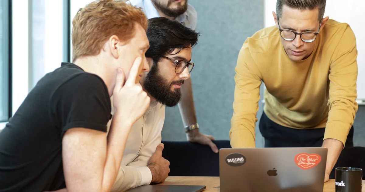 a group of men sitting around a table looking at a laptop