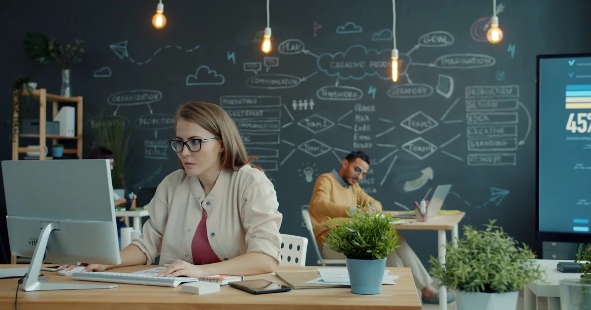 Woman working on computer in modern office with chalkboard.