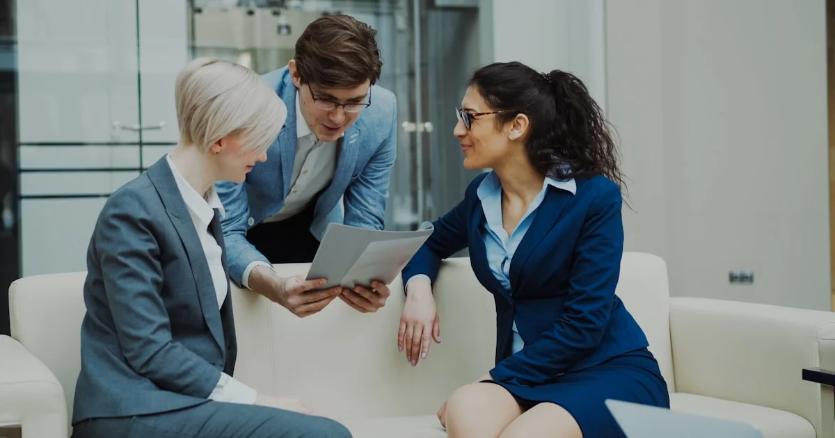 Three business people in suits discussing documents.