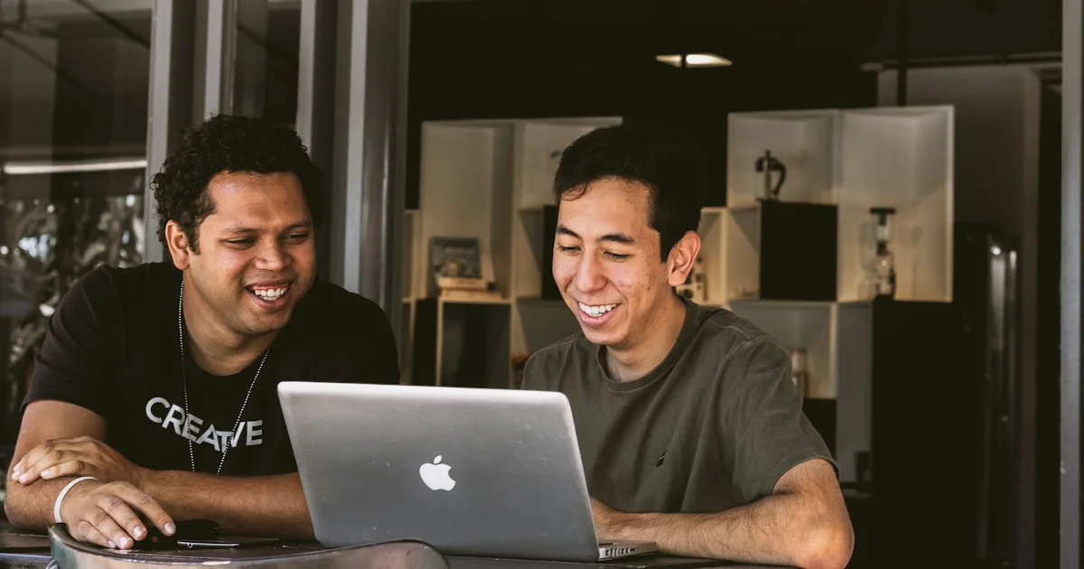 two smiling men looking at MacBook