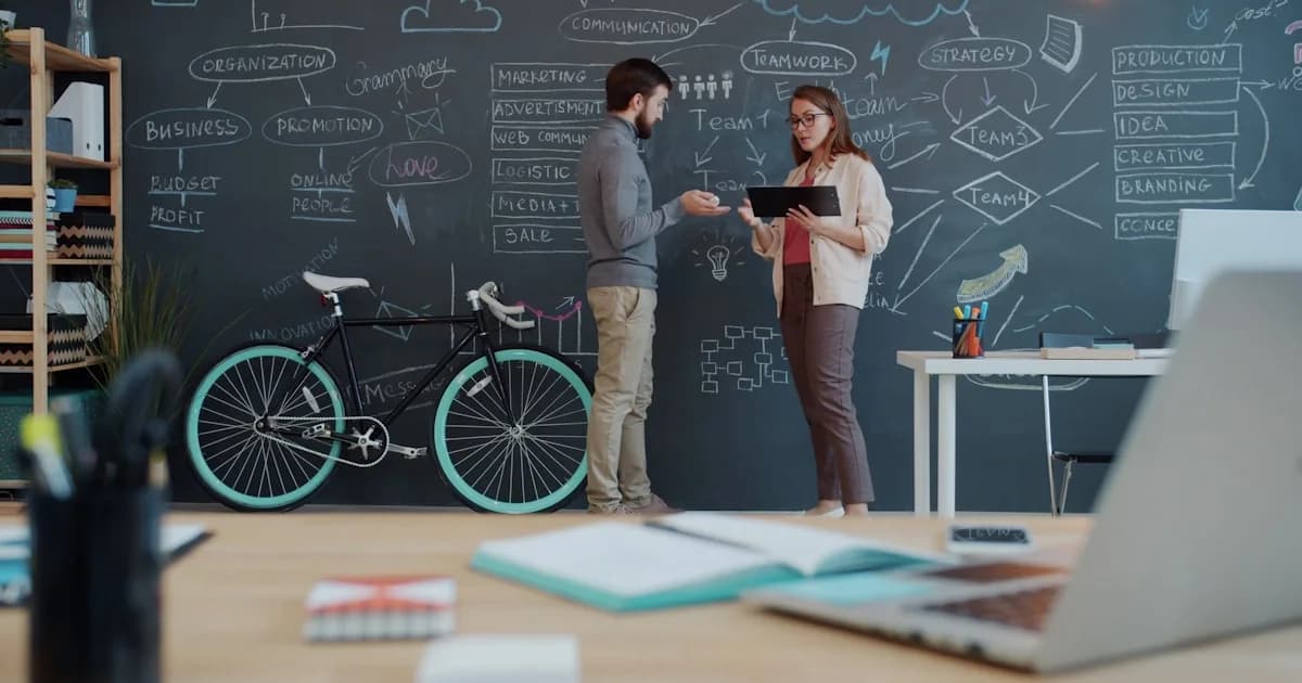 Two people discuss a plan on a chalkboard wall.