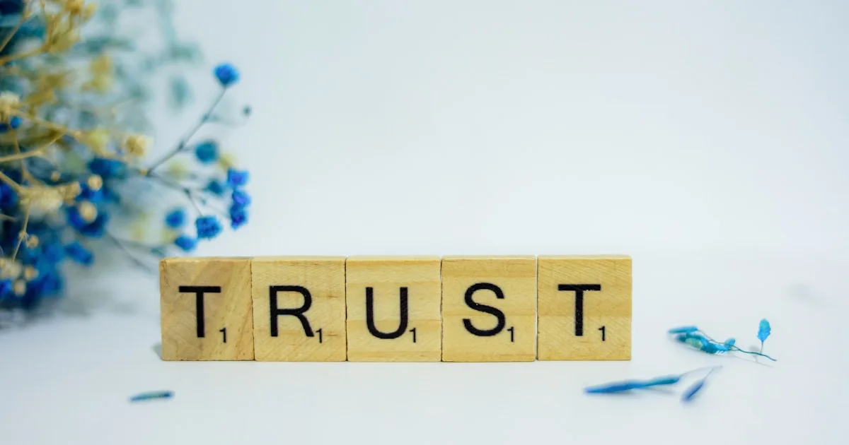 A wooden block that says trust, surrounded by blue flowers