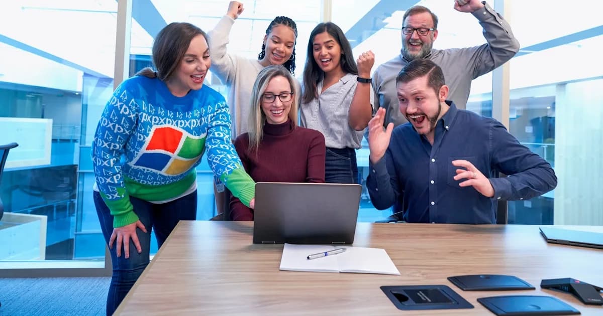 men and women sitting and standing by the table looking happy while staring at laptop
