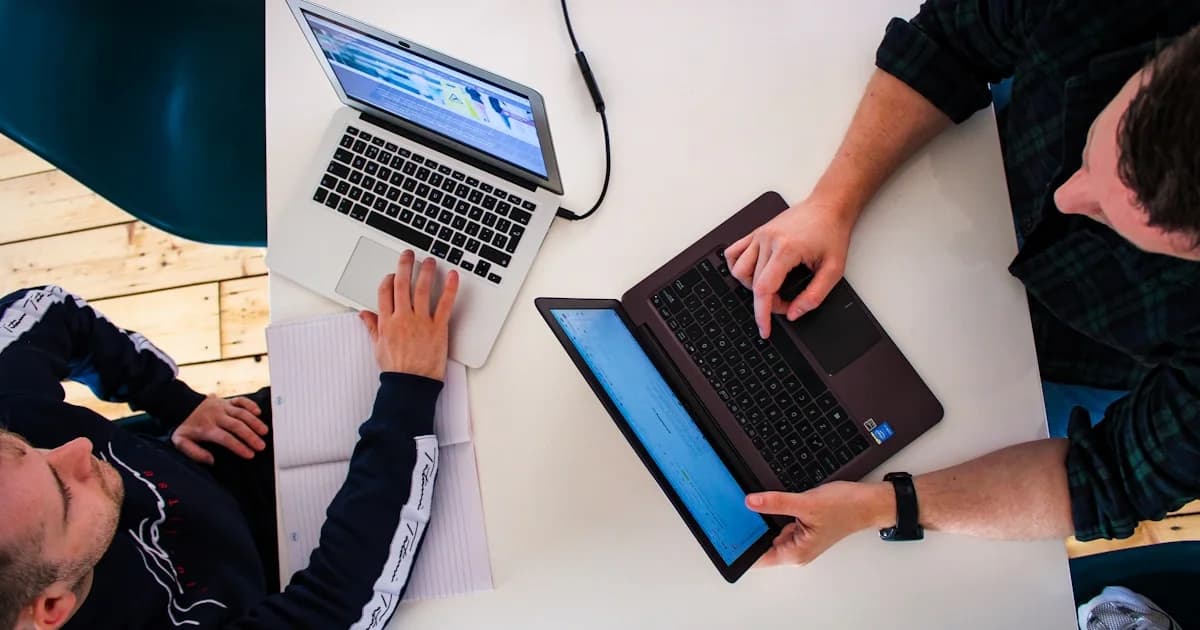 two men sitting at a table working on laptops