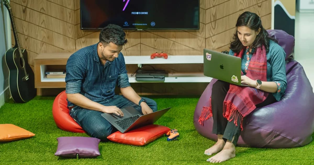 a man and a woman sitting on bean bag chairs looking at a laptop