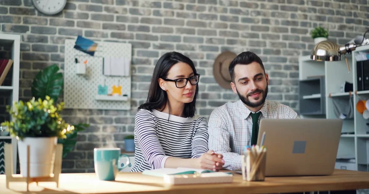 a man and woman sitting at a table looking at a laptop
