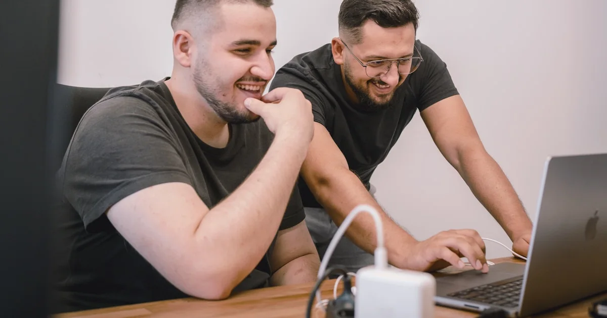 two men sitting at a table looking at a laptop