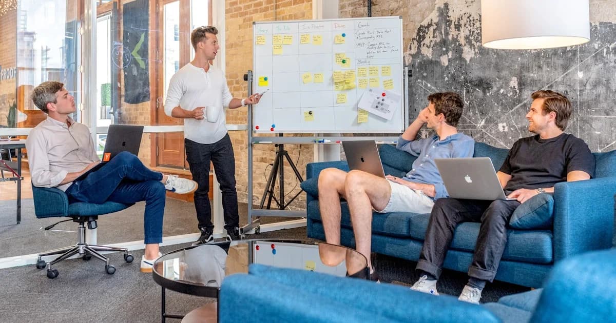 three men sitting while using laptops and watching man beside whiteboard