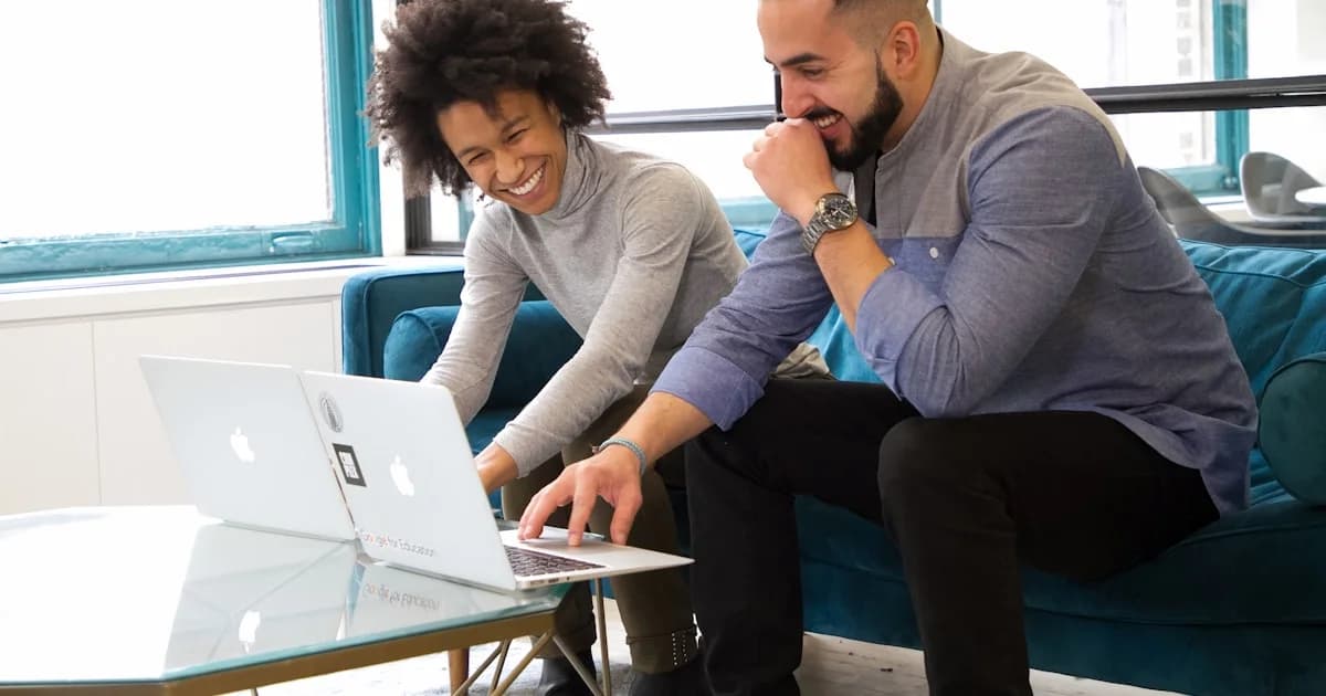 a man and woman sitting on a couch looking at a laptop
