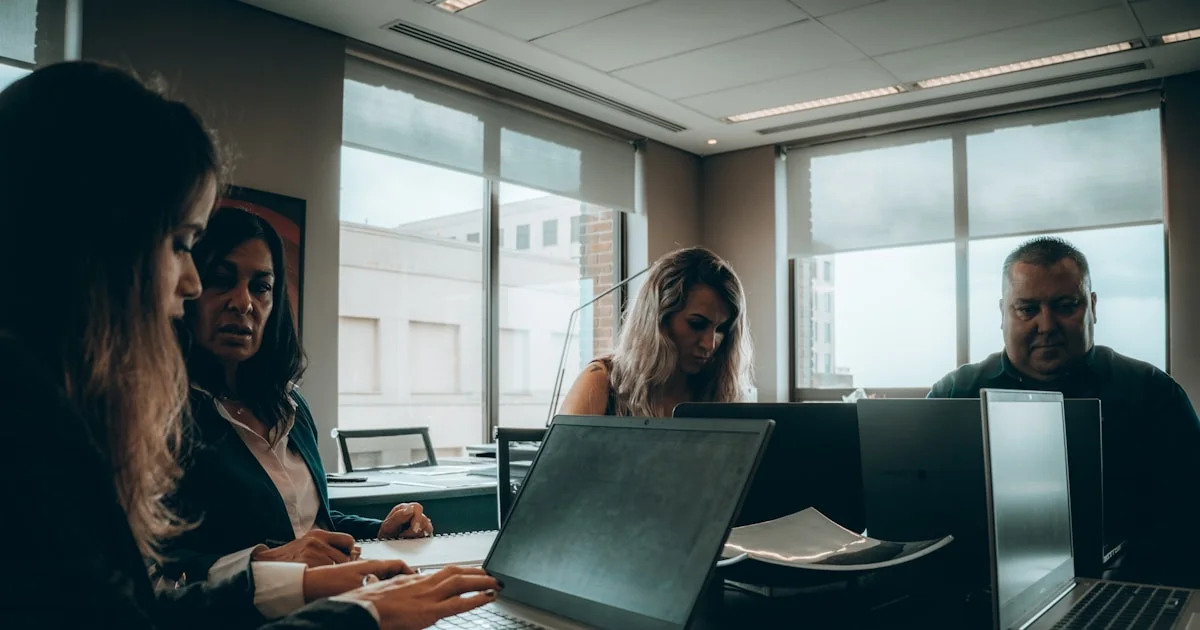 a group of people sitting around a table with laptops
